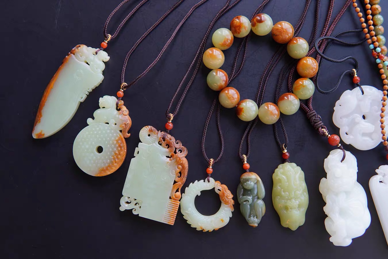 M&T Jewelry carved jade pendants and a bracelet displayed on a dark surface