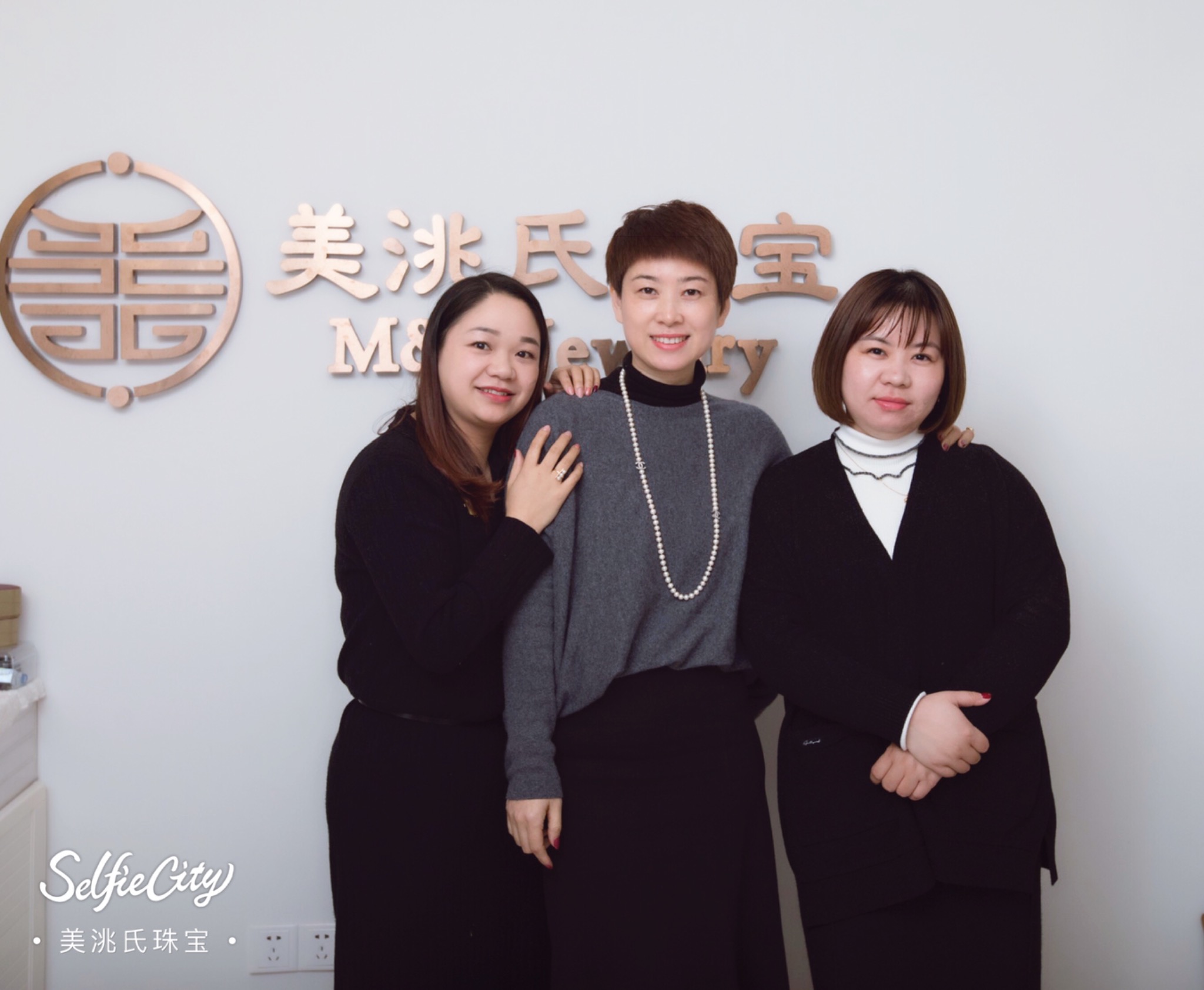 The three women behind M&T Jewelry together in front of the brand sign